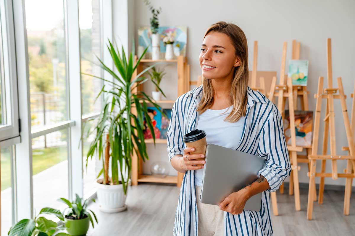 Femme dans un atelier créatif qui réfléchit, avec un café et un ordinateur portable