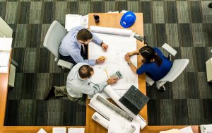 Vue de dessus de trois personnes étudiant des plans techniques autour d'une table