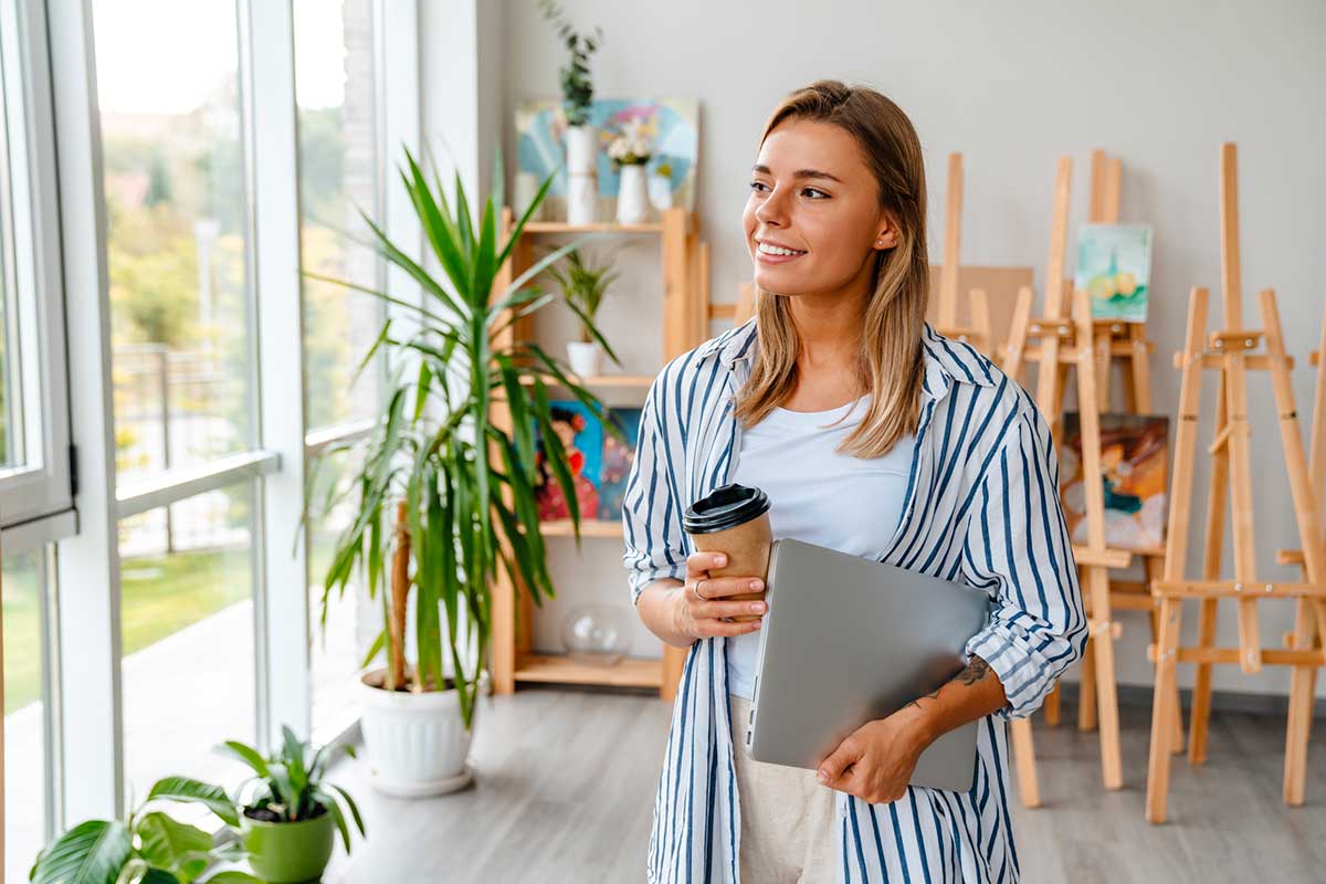 Femme dans un atelier créatif qui réfléchit, avec un café et un ordinateur portable