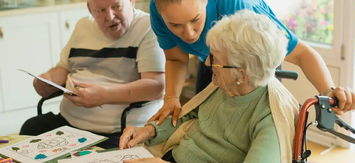 Aide-soignante accompagnant deux personnes âgées dans une activité de coloriage