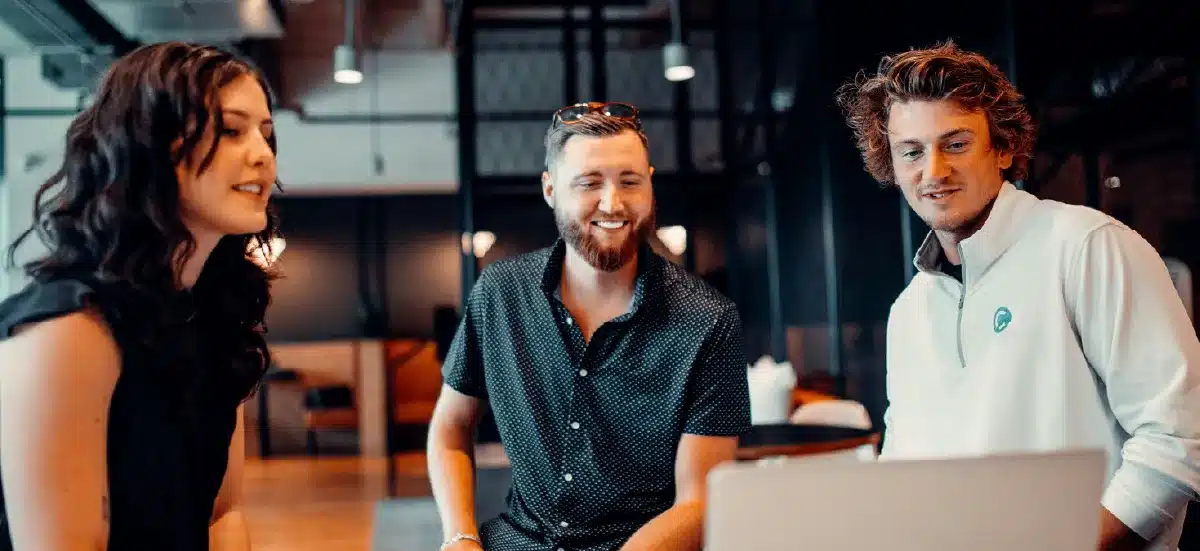 Trois collègues souriants échangent autour d'un ordinateur portable dans un espace de coworking