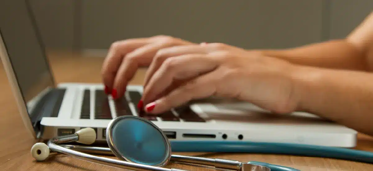 Mains d'une professionnelle de santé tapant sur un ordinateur portable, stéthoscope au premier plan