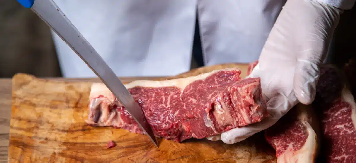 Boucher tranchant de la viande de bœuf sur une planche en bois