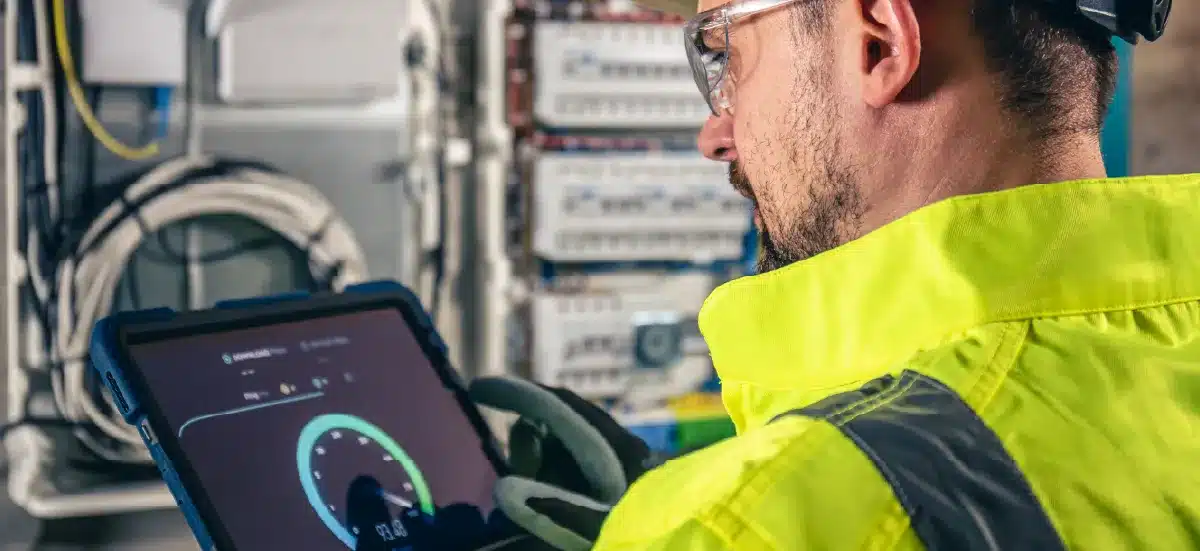 Technicien en gilet haute visibilité consultant une tablette devant un tableau électrique