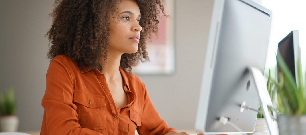 Femme en chemise orange travaillant devant un écran d'ordinateur