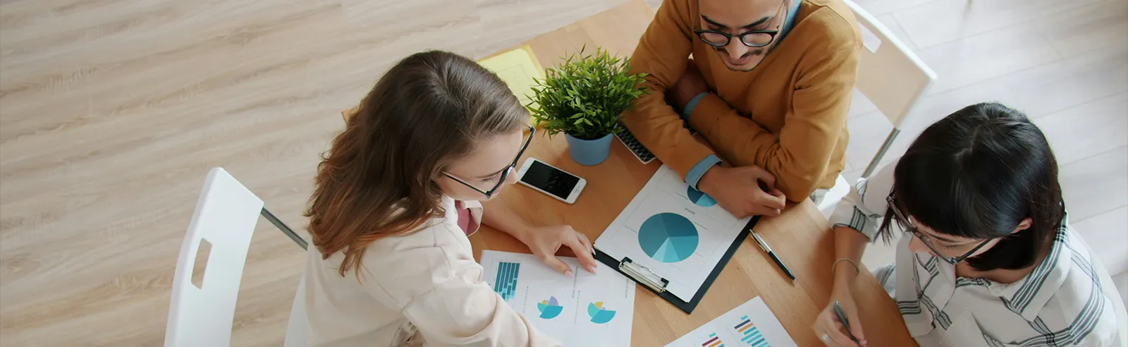 Vue de dessus de trois collègues analysant des graphiques imprimés autour d'une table