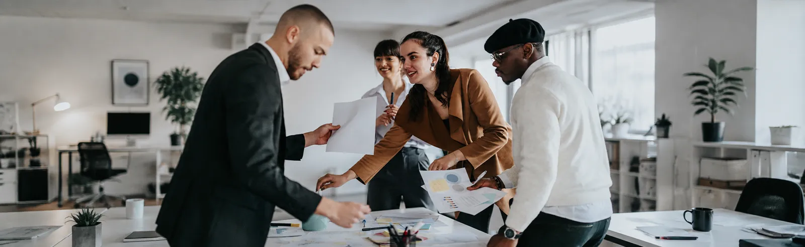 Quatre collègues debout autour d'une table de travail couverte de documents