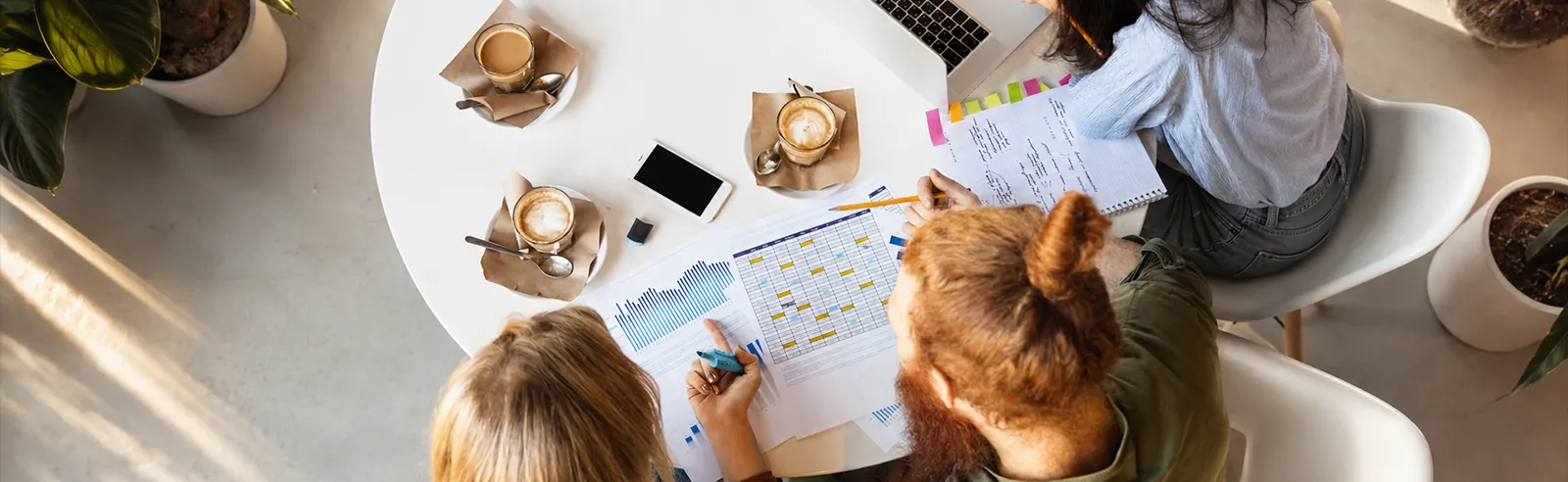 Vue de dessus de trois personnes autour d'une table avec documents et cafés
