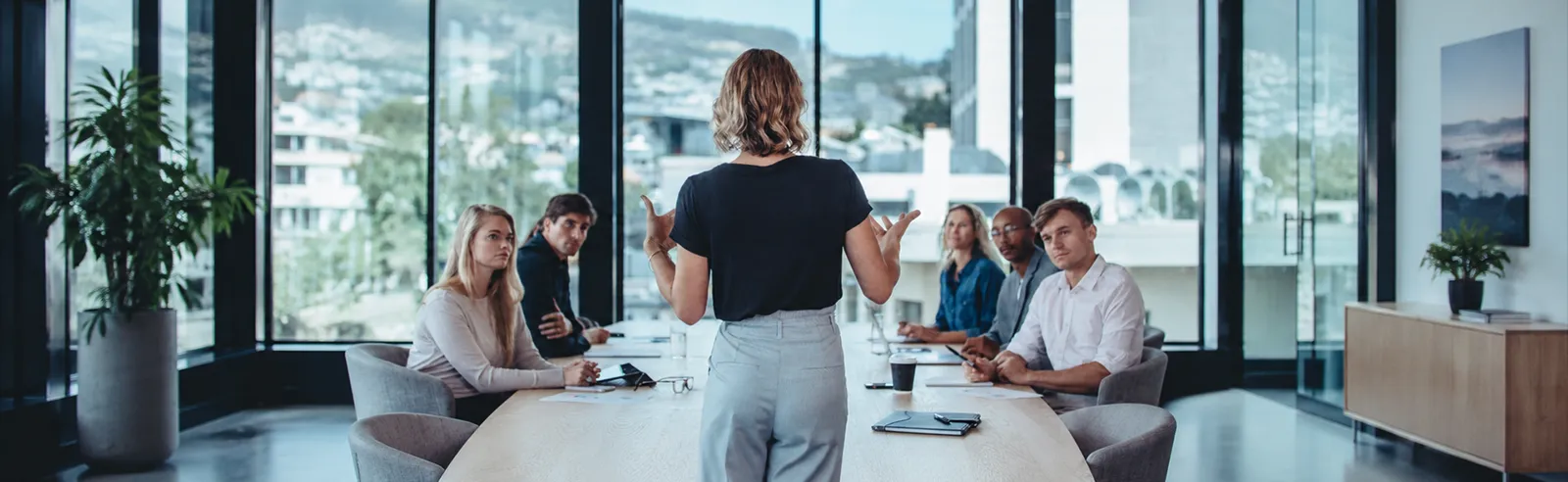 Personne debout s'adressant à six participants autour d'une table de réunion