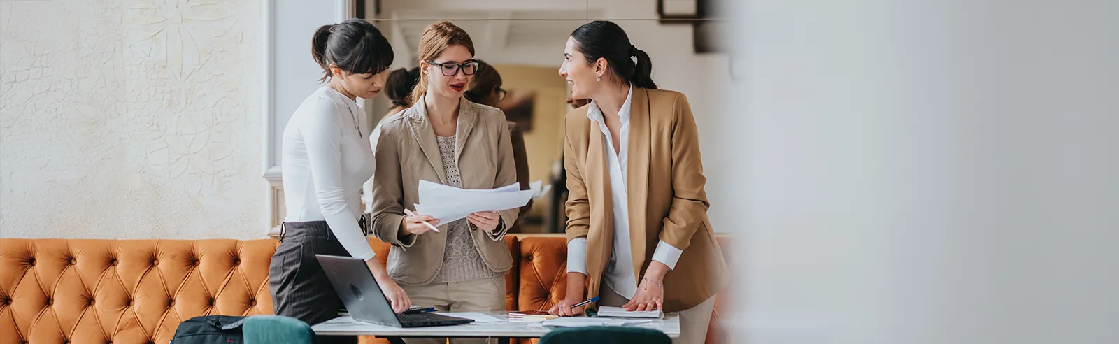 Trois collaboratrices debout autour d'une table avec documents et ordinateur portable